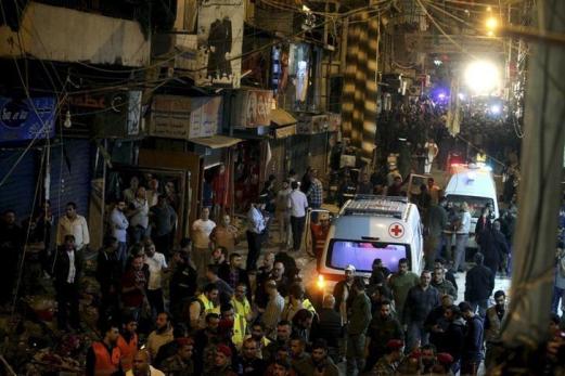 Red Cross vehicles drive by as residents and Lebanese army members inspect a damaged area caused by two explosions in Beirut's southern suburbs, Lebanon