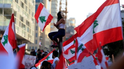 A demonstrator sits on a pole while carrying a national flag during an anti-government protest in downtown Beirut_ Lebanon October 20_ 2019_Ali Hashisho_Reuters